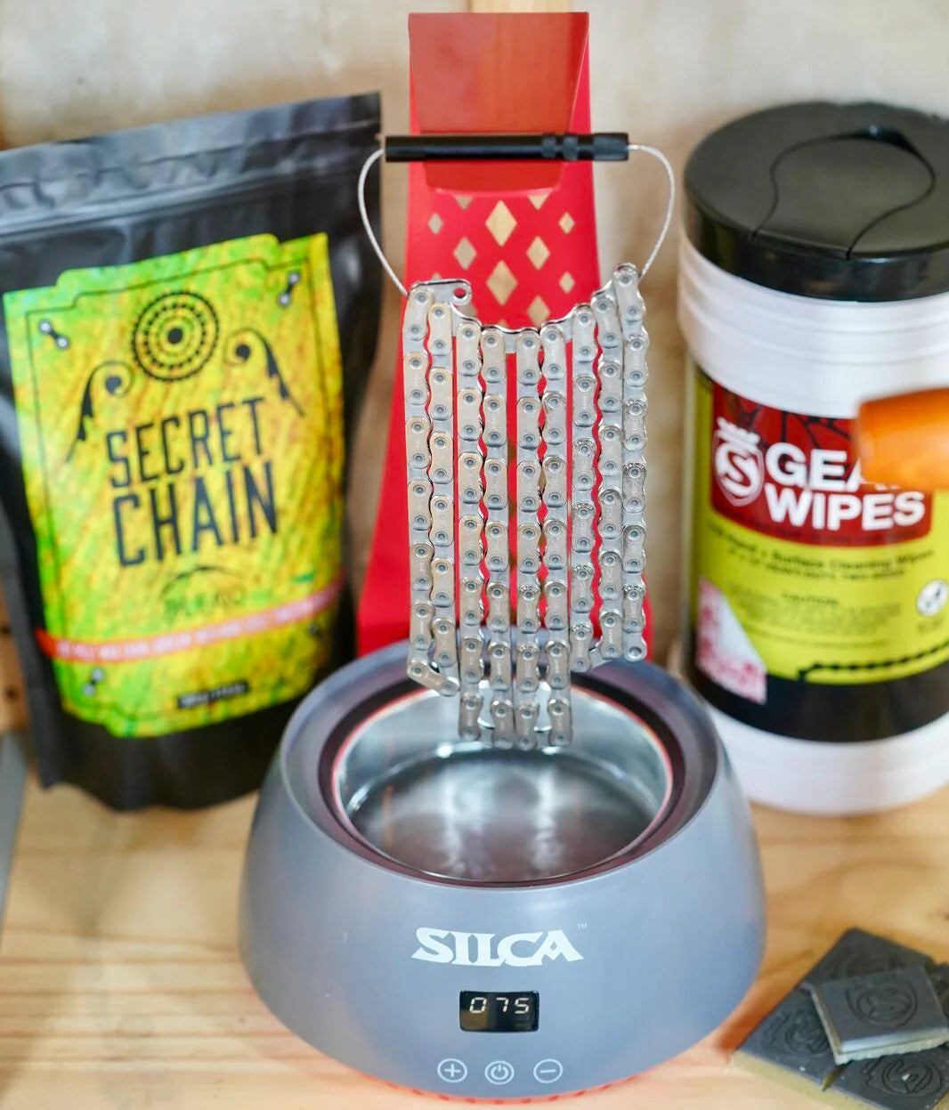 Silca Bicycle Chain Waxing Pot with chain hanging on the stand on a wooden workbench.